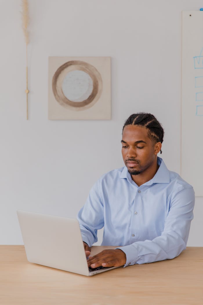 Services A professional man with braided hair working on a laptop in a modern office setting.