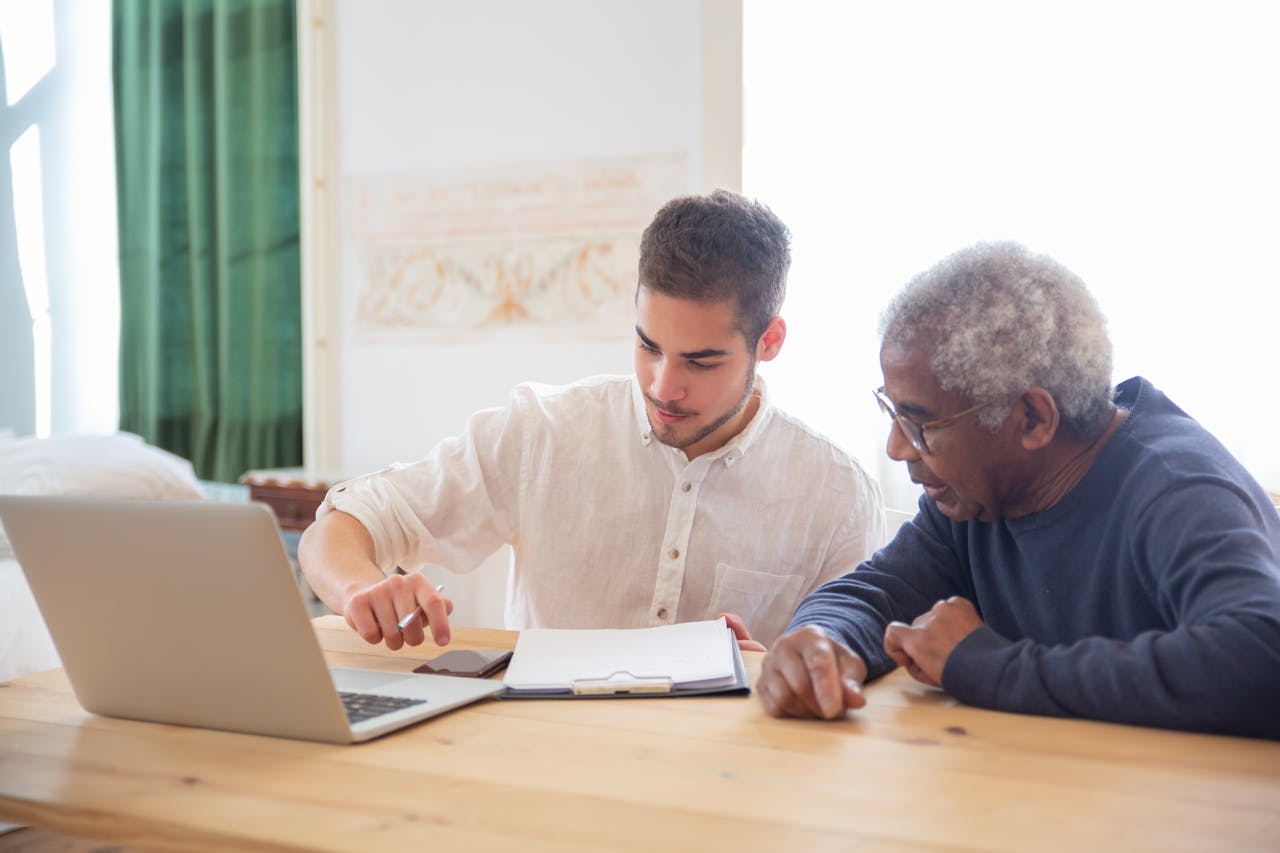 Services Young man teaches elderly gentleman to use technology at home.